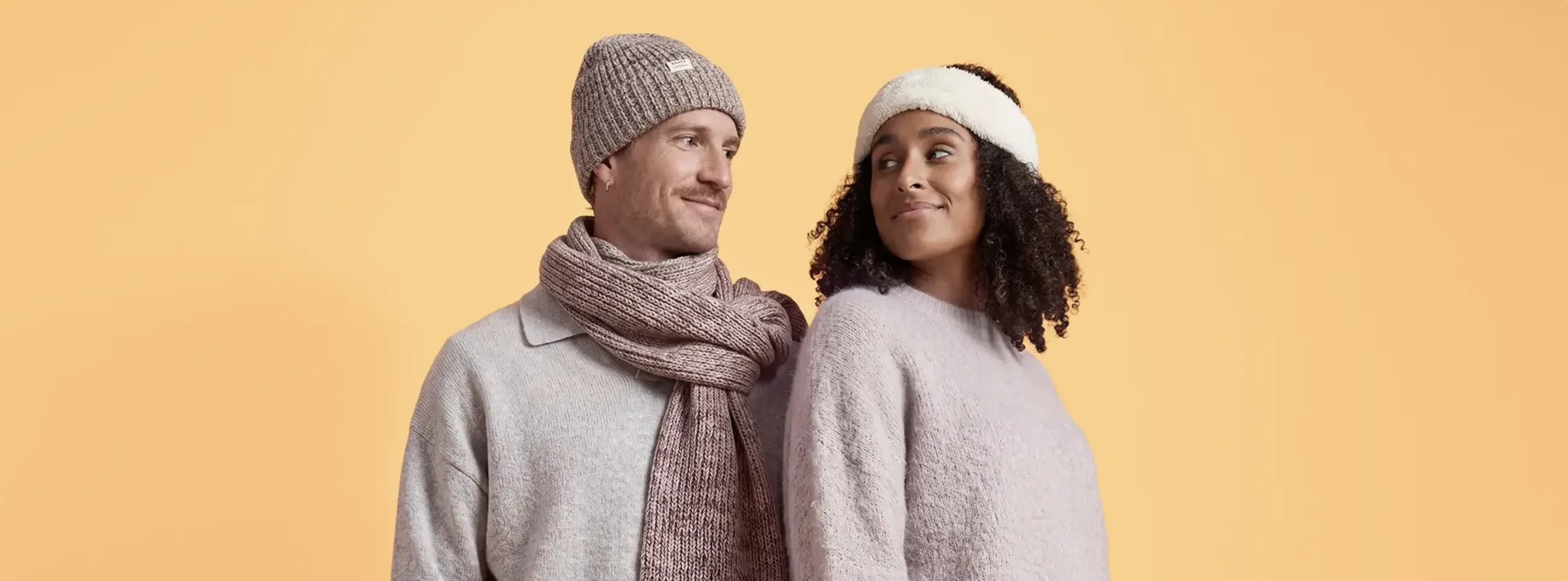 Twee modellen in winterse knitwear tegen de warme gele achtergrond van de bol-campagne